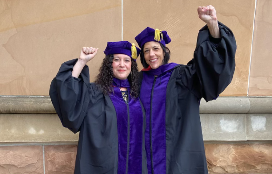 graduates in cap and gown with hands raised