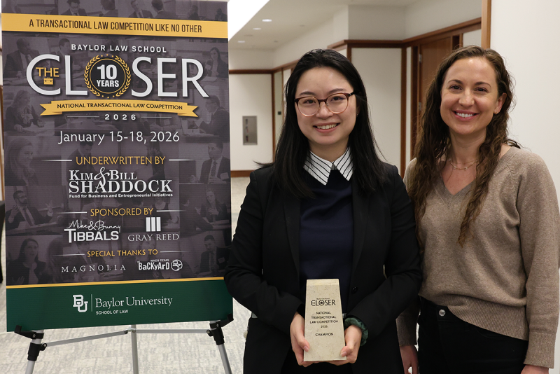 Two individuals standing to the right of signage about The Closer Competition, smiling and holding a trophy