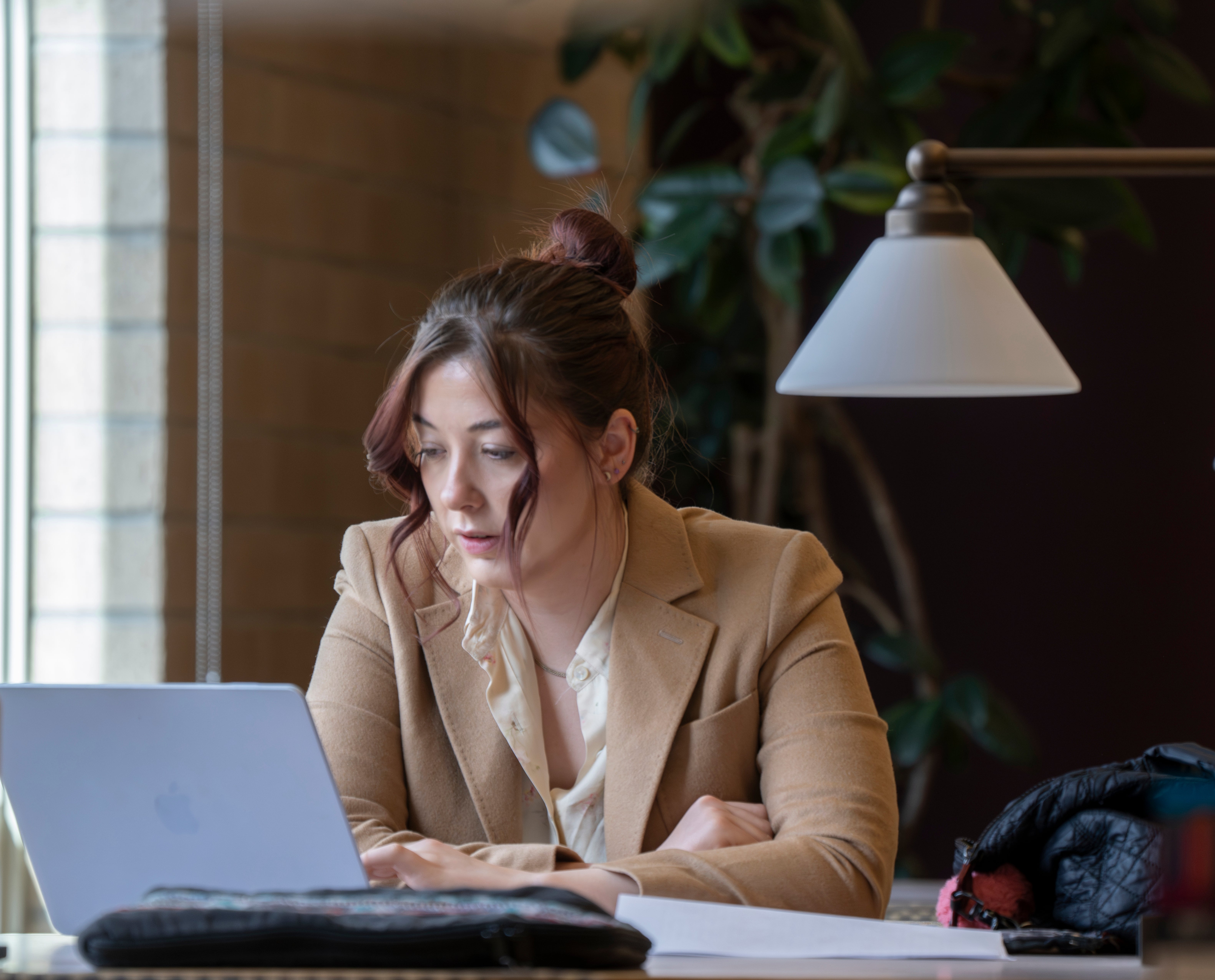 A female law student wearing a blazer works at a laptop computer in a law library.